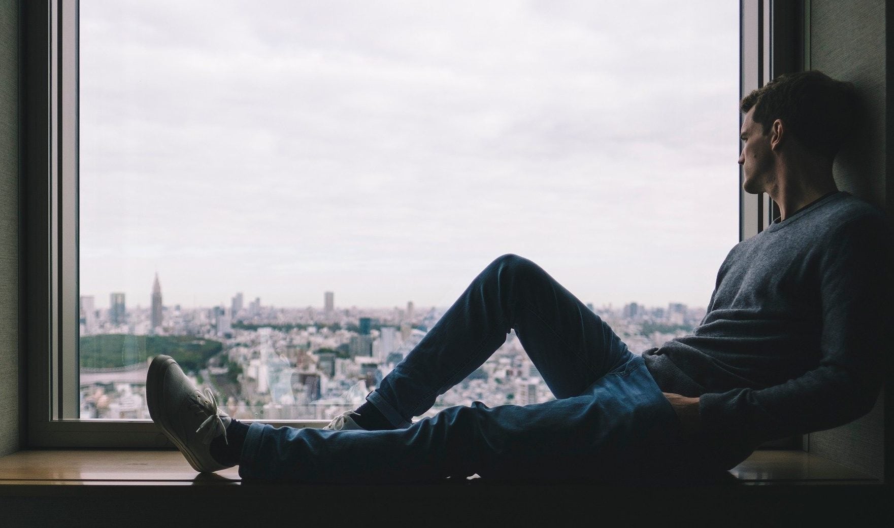 A man sits and looks out a window out to a skyline.