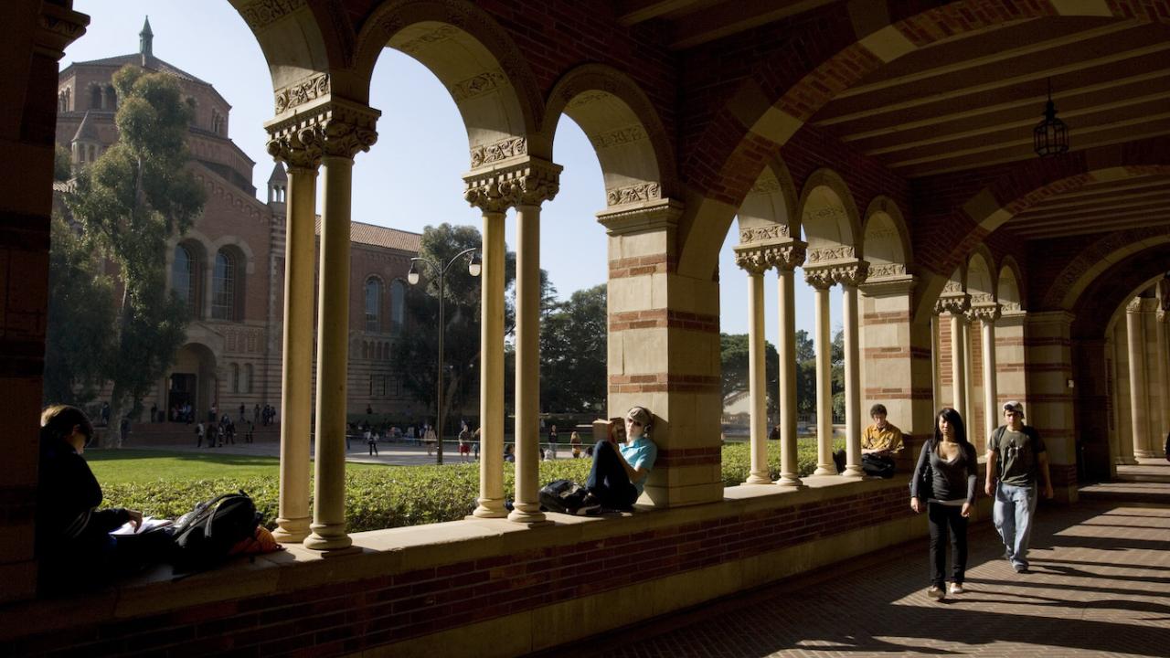 A person sits in a shaded UCLA walkway.